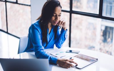 Woman in blue shirt using tablet next to bright office windows, Automating ceded insurance process | DXC Technology Insights